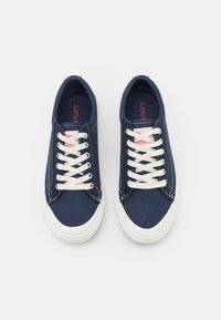 Marinblå canvas-sneakers med vita gummisulor och snörning, med en röd logotagsdetalj och kontrasterande söm på sidorna.