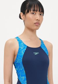 Navy one-piece swimsuit featuring a blue and green bird-patterned design on the straps and sides, made of smooth, stretchy fabric.