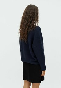 Navy-blauer Strickpullover mit lockerer Passform und geripptem Textur, kombiniert mit einem schwarzen, gerippten Minirock. Sichtbare lange, lockige Haare.