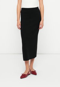 Jupe noire en tricot de longueur médiane avec une taille côtelée, associée à des ballerines rouges brillantes avec des nœuds et un design de bout allongé.