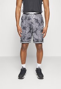 Shorts noirs avec un motif corail blanc, comportant une taille élastique avec cordon de serrage et des bandes latérales contrastées. Associés à des baskets noires et des chaussettes blanches.