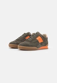 Dunkelgrüne Wildleder-Sneaker mit einem orangefarbenen Akzent, ausgestattet mit einer Gummisohle, Schnürdesign und einem gepolsterten Innenraum.