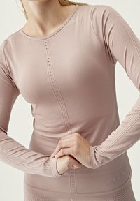 Långärmad sporttop i ljusrosa, med en texturerad frampanel med knappar, subtila sömnadsdetaljer och figursydda ärmar.