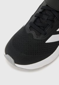 Baskets noires de sport avec un dessus en mesh texturé, des lacets plats et un accent blanc sur la semelle avec un design de bout arrondi.