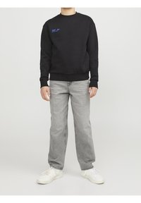 Svart bomullssweatshirt med blå broderad text, rund halsringning, ribbade ärmslut och fåll. Kombinerad med grå denimjeans och vita sneakers.