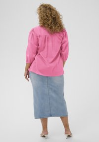 Blouse rose à manches bouffantes avec détail froncé dans le dos, associée à une jupe en jean longueur midi délavée clair, présentant une coupe ample et un style décontracté.