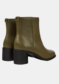 Botas de tobillo de cuero verde oliva con una superficie texturada, punta redondeada y tacón cuadrado. Con pestañas en la parte trasera para ponérselas fácilmente.
