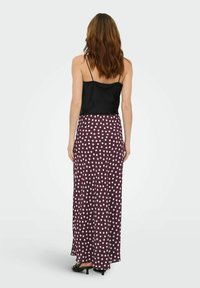 Camisole en satin noir associée à une longue jupe prune avec des pois blancs. La jupe a une coupe fluide et descend jusqu'aux chevilles.