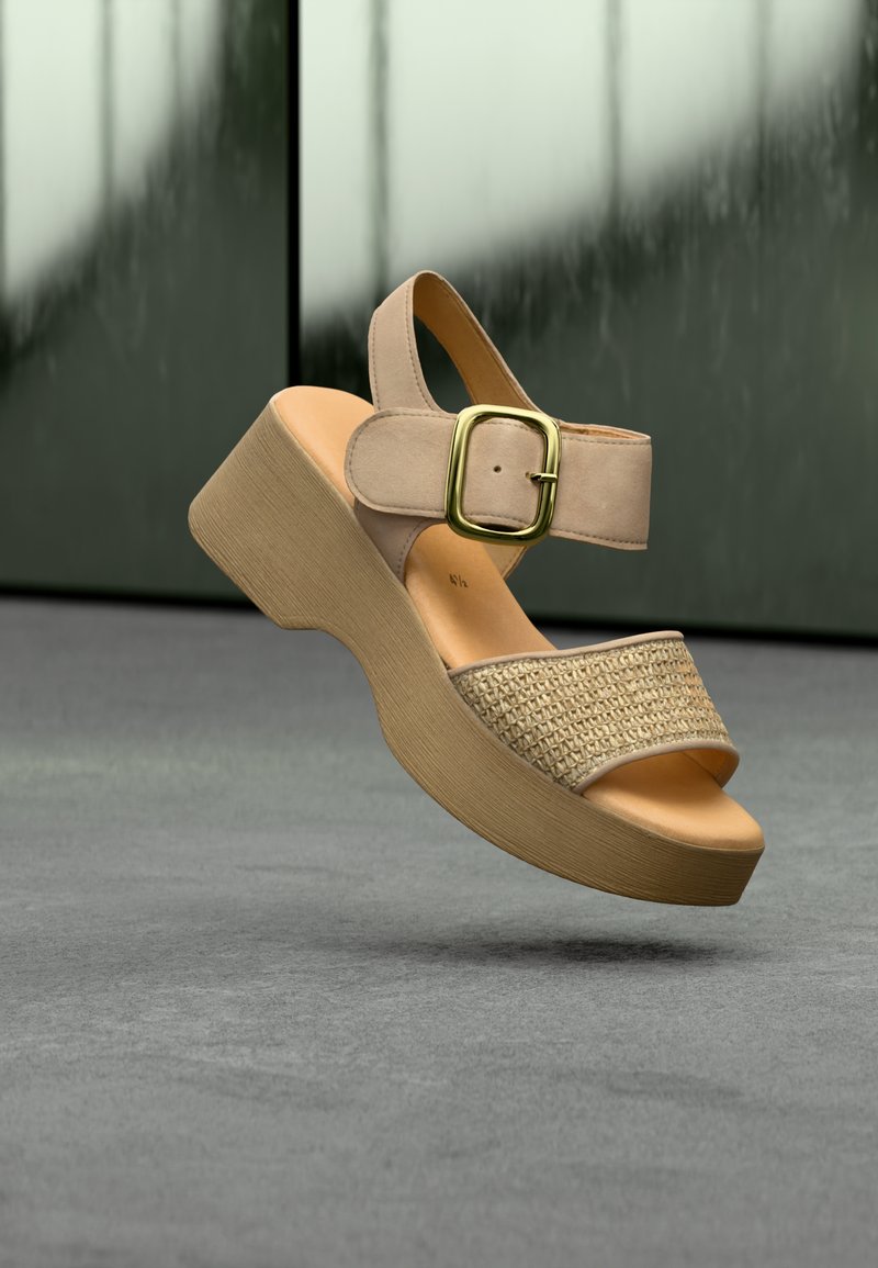 Μπεζ πλατφόρμα σανδάλι με υφασμένο λουρί, ρυθμιζόμενο πόρπη στον αστράγαλο και καμπυλωτό ξύλινο τακούνι. Ομαλή σόλα και μίνιμαλ σχεδιασμός.