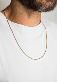 Un colier din metal auriu este expus pe o persoană care poartă un tricou alb. Colierul are un design subțire, neted și cu zale interconectate.
