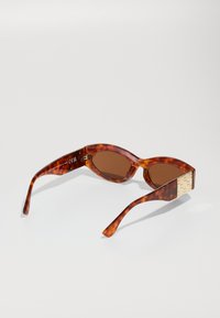 Brown tortoiseshell sunglasses with oval lenses, a thick frame, and a textured gold accent on the temple for a distinctive detail.