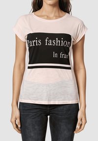 Camiseta rosa claro con un diseño gráfico negro que presenta el texto blanco "Paris fashion In frare." Tienen mangas cortas y cuello redondo. Diseño casual.