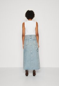 Denim maxiskjørt med en lys blå vask, som har en tettsittende midje, store baklommer og frynse-detaljer i kanten. Kombinert med en hvit topp.