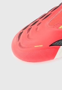 Κοντινό πλάνο της κόκκινης αθλητικής κάλ τσας Adidas Nanostrike με υφή επιφάνειας και μαύρες και κίτρινες λεπτομέρειες σχεδίασης.