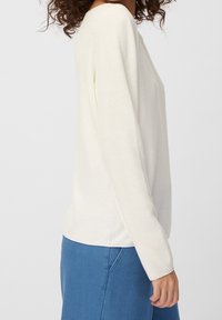 Ljuskrämfärgad stickad tröja med långa ärmar och en avslappnad passform. Texturen är mjuk och den har ett subtilt, vävt mönster.