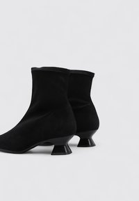 Bottines en suédine noire avec une silhouette sculptée et des talons cylindriques évasés. Texture lisse et design sans couture.
