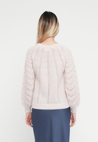 Jasnoróżowy sweter dzianinowy z balonowymi rękawami, z wzorem zygzakowym i pionowymi wycięciami, ściągacz u dołu i przy mankietach.