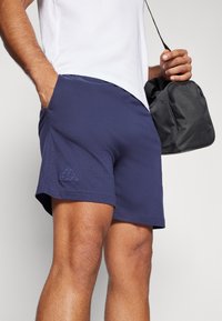 Bermudas deportivas de color azul marino fabricadas con tejido ligero, con bolsillos laterales y un pequeño logotipo bordado cerca del dobladillo.
