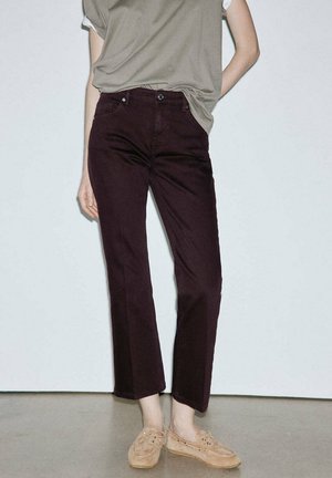 Personne portant un pantalon droit violet foncé, des mocassins beiges sans lacets et un haut sans manches vert olive rentré.