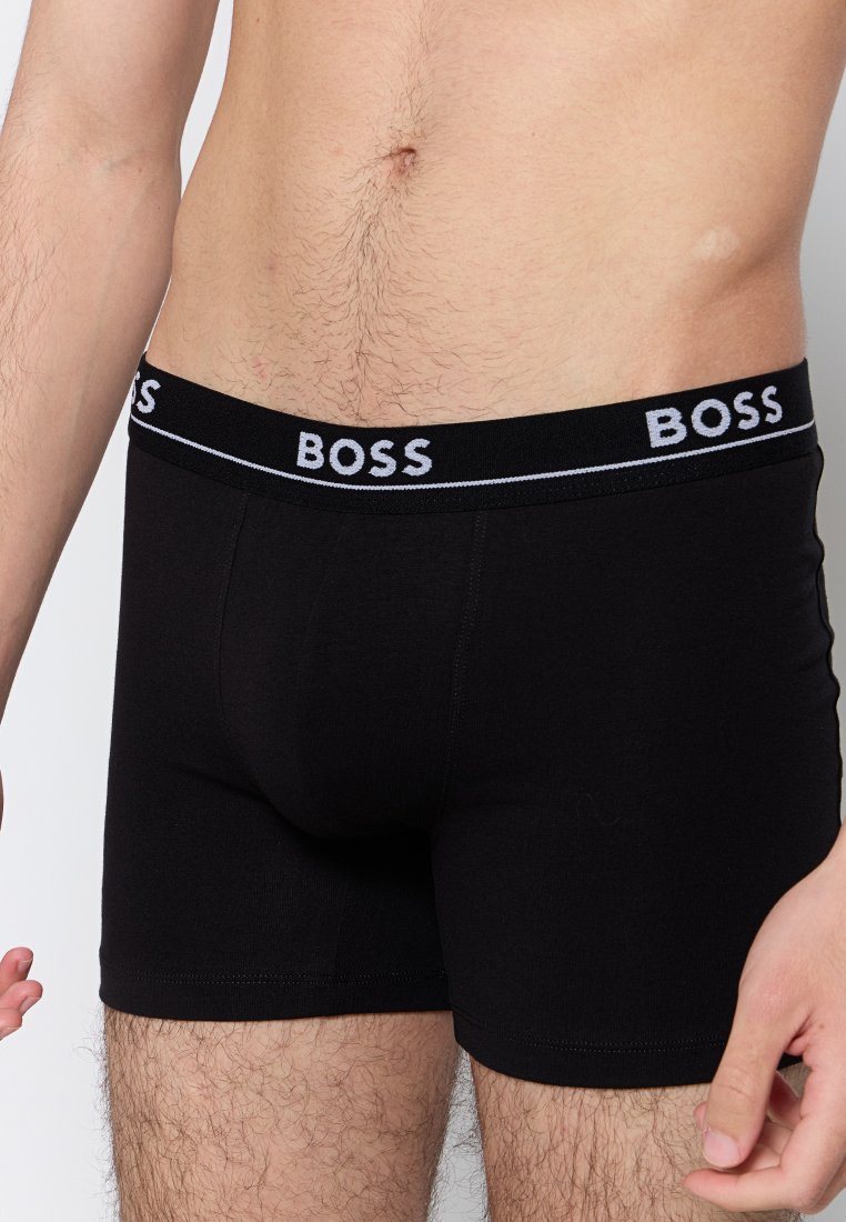 Boxers noirs avec une ceinture élastique douce comportant le texte "BOSS" en blanc. Fabriqués en tissu lisse, design ajusté.