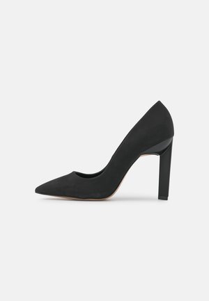 Escarpin noir en daim avec un bout pointu, texture lisse et un large talon bloc. Design minimaliste sans motifs ni accents visibles.