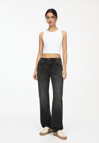 Witte mouwloze crop top, zwarte wijde jeans, lichtgekleurde sneakers, gladde textuur, vijf-pocket ontwerp en subtiele naden.