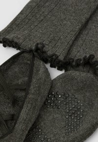 Grå stickade leggings med volangkanter och ett matchande par strumpliknande skor med en texturerad, greppförbättrad sula.
