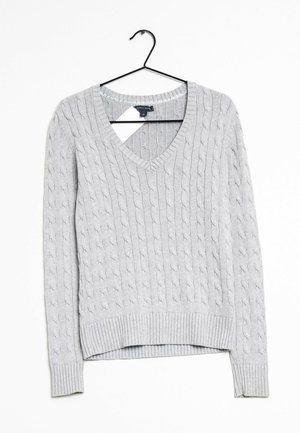 Maglione grigio lavorato a maglia con scollatura a V, polsini e orlo a costine. Presenta un motivo testurizzato su tutta la superficie. Appeso a un gancio nero.