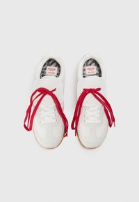White sneakers with a textured pattern, red laces, and rubber soles, featuring a black and white patterned interior and logo tags.