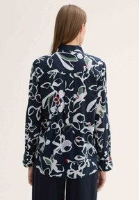 Navy blouse with long sleeves, floral pattern in white, green, and red, soft fabric, slight shine, buttoned cuffs, and back yoke detail.