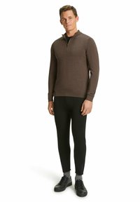 Brauner Reißverschlusspullover mit hohem Kragen, kombiniert mit schwarzen, schmalen Hosen und schwarzen Sneakers. Geschmeidige Textur und enge Passform.