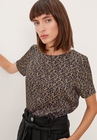 T-shirt nera a maniche corte con motivo astratto dorato, scollatura rotonda e vestibilità comoda. Abbinata a pantaloni neri a vita alta.