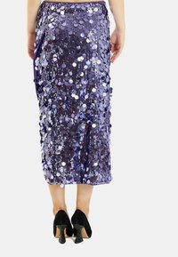 Fioletowa spódnica cekinowa o dopasowanej sylwetce, z dużymi i małymi cekinami oraz bocznym rozcięciem. Nosi się ją z czarnymi butami na obcasie.