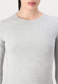 Haut à manches longues de couleur gris clair, fabriqué à partir d'un tissu doux et texturé, avec un col rond et une silhouette ajustée.