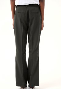 Tmavě zelené kalhoty na míru se střihem rovného nohu, s dvěma zadními kapsami a hladkou texturou. Nosené s bílým topem a podpatky.