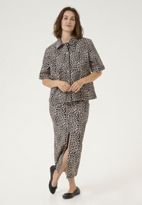 Dvoudílný outfit skládající se z krátkého rukávu košile s leopardím potiskem a odpovídající sukně ke kolenům s předním rozparkem. Černé baleríny.
