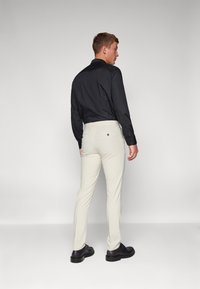 Férfi öltözet fekete gombos inggel és világos bézs nadrággal. Az ing sima tapintású; a nadrág testreszabott, slim fit stílusú.