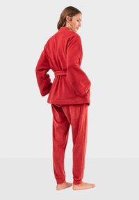 Conjunto de loungewear de lana roja con un albornoz con cinturón y pantalones con estampado, que presenta una textura suave y sutiles acentos de puntos en la tela.