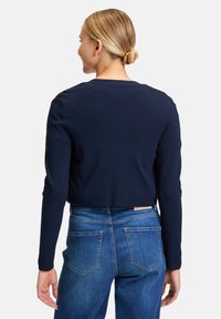 Pullover navy corto con maniche lunghe, texture a costine e scollatura a girocollo, abbinato a jeans in denim blu con tasche posteriori.