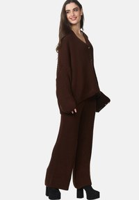 Ensemble de pull en laine marron avec décolleté en V, coupe décontractée et manches longues. Le pantalon est à jambe large avec une texture côtelée. Chaussures à plateforme noires.