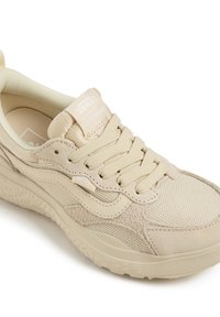 Beige lenkkarissa on verkkokangasta ja mokkanahkaa, kuminen pohja ja litteät nauhat. Siinä on kantaosa vetotappi ja merkkilogo kielen etuosassa. Pohjan muotoilu on teksturoitu.