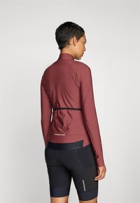 Burgunderfarget langermet topp med høy krage, slim passform og reflekterende detaljer, kombinert med svarte sykkelshorts med mesh-detaljer og lommer.