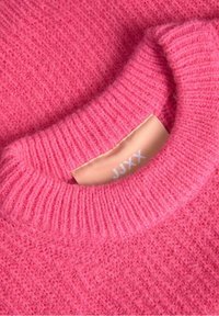 Puszysty różowy sweter z prążkowanym kołnierzem, z kremową metką z logo "JJXX". Miękka tekstura z delikatnym wzorem.