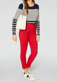 Pantalons ajustés rouges associés à un haut à manches longues rayé bleu marine et blanc. Accessoirisés avec un sac à main blanc et des basket blanches.