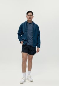 Felpa con zip blu scuro e cordini, indossata sopra una t-shirt abbinata, abbinata a pantaloni corti neri e scarpe da ginnastica bianche. Design atletico semplice.