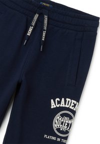 Pantalones de chándal jogger azul marino fabricados en tejido suave, con bolsillos laterales, una cinturilla elástica y texto y diseños impresos en blanco.