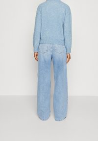 Helles, glitzerndes Sweatshirt mit tailliertem Schnitt und langen Ärmeln, kombiniert mit hochgeschnittenen, weit geschnittenen hellblauen Jeans. Rückansicht gezeigt.