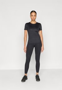 Μαύρο αθλητικό σύνολο που αποτελείται από κοντομάνικη εφαρμοστή μπλούζα και αθλητικό κολάν χωρίς ραφές, και τα δύο από λείο, ελαστικό ύφασμα.