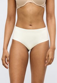 Εσώρουχο με ψηλή μέση σε κρεμ απόχρωση, φτιαγμένο από λείο υλικό, με ελάχιστες ραφές και διακριτικό λογότυπο της μάρκας στη μέση.