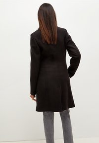 Svart yllekappa med en strukturerad design, långa ärmar och rak passform. Har sidofickor och en längd som når till mitten av låret.